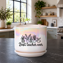 A white ceramic planter pot with a matching saucer sits on a dark kitchen countertop. The pot has an iridescent sheen and is printed with a black graphic of potted plants and the text 'Best teacher ever'.