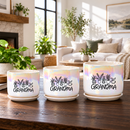 A white ceramic planter pot with a saucer, featuring a black graphic of potted plants and the word 'GRANDMA' in script, set on a wooden table in a bright, modern living room.