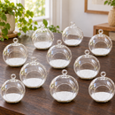 close-up view of three mini flat-bottom hanging glass terrariums with white sand and dark sand varieties, showing the hanging loop and clear glass construction, styled on a wooden shelf