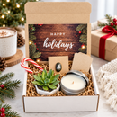 close-up view of opened christmas cheer deluxe gift box revealing live succulent in small ceramic pot, goat milk lotion bottle, rustic ornament, prayer card pack, and holiday-themed packaging with warm holiday aesthetic