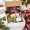 close-up view of opened christmas cheer deluxe gift box revealing live succulent in small ceramic pot, goat milk lotion bottle, rustic ornament, prayer card pack, and holiday-themed packaging with warm holiday aesthetic