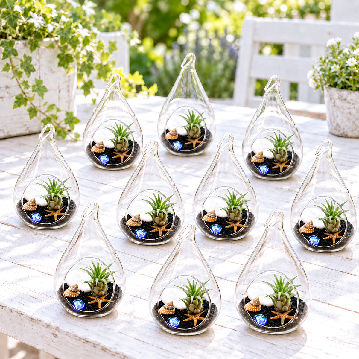 ten small teardrop-shaped glass terrariums filled with black sand and tiny succulents arranged in a group on a white surface