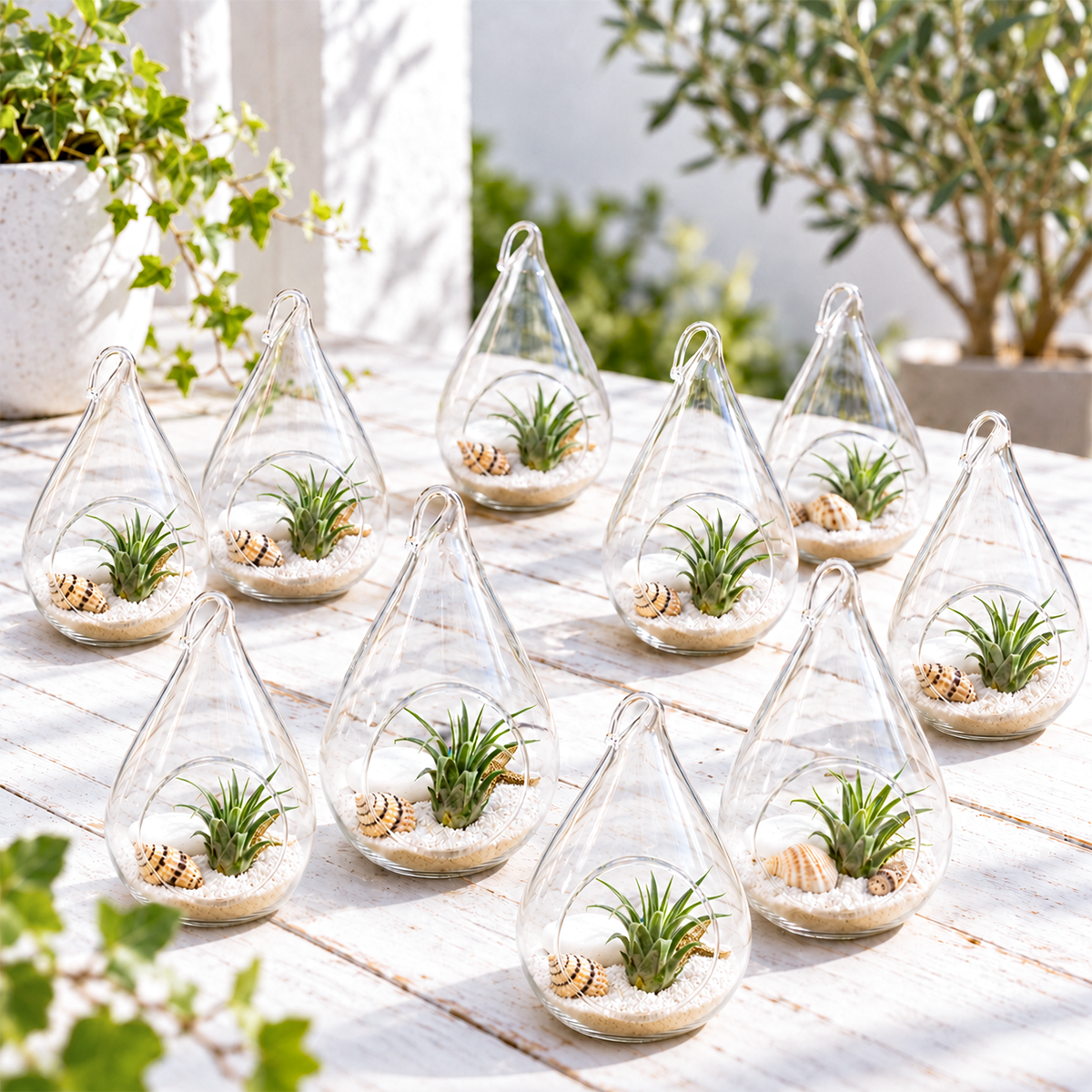 ten small teardrop-shaped glass terrariums filled with white sand and miniature green plants, arranged in a grouped display on a neutral surface