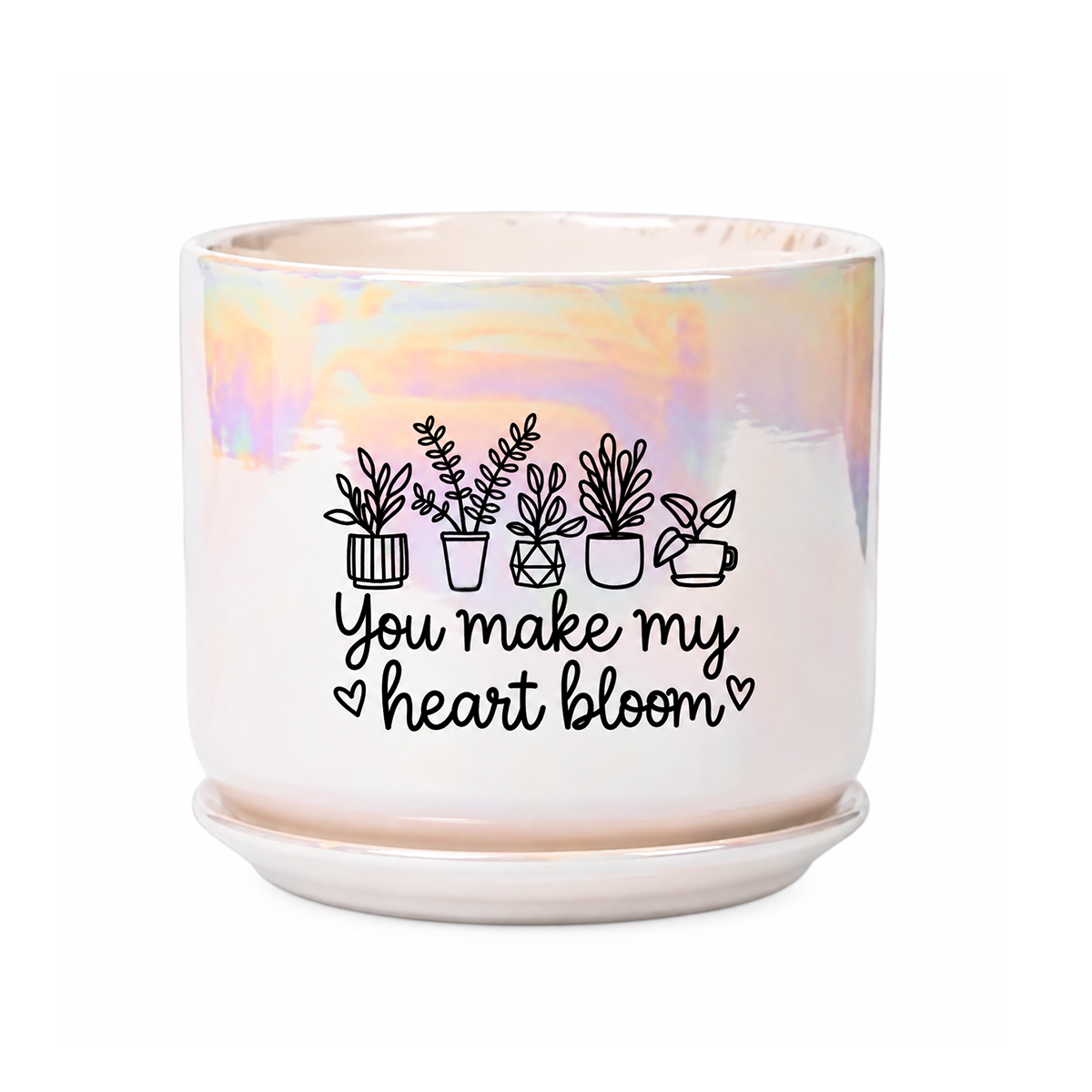 A white ceramic planter pot with a matching saucer, featuring an iridescent pastel sheen and a black graphic of potted plants with the text 'You make my heart bloom'.